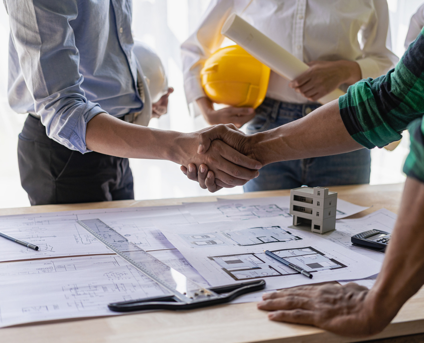 Side view of construction workers looking over blueprint and shaking hands