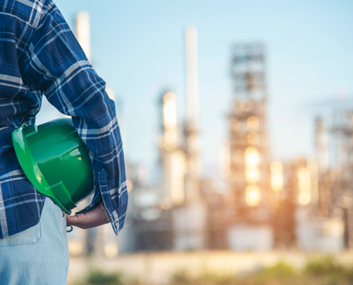 Back view of a female construction worker looking at construction site, holding green hard hat on her hip